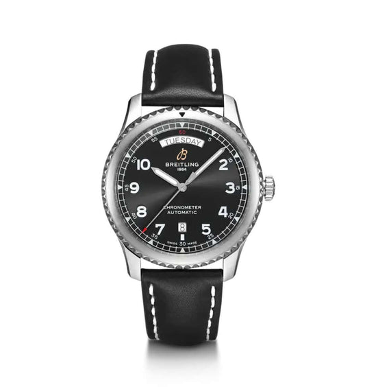 A Breitling Aviator 8 Automatic with a stainless steel case, black dial featuring white Arabic numerals, day and date window, and a black leather strap with white stitching.